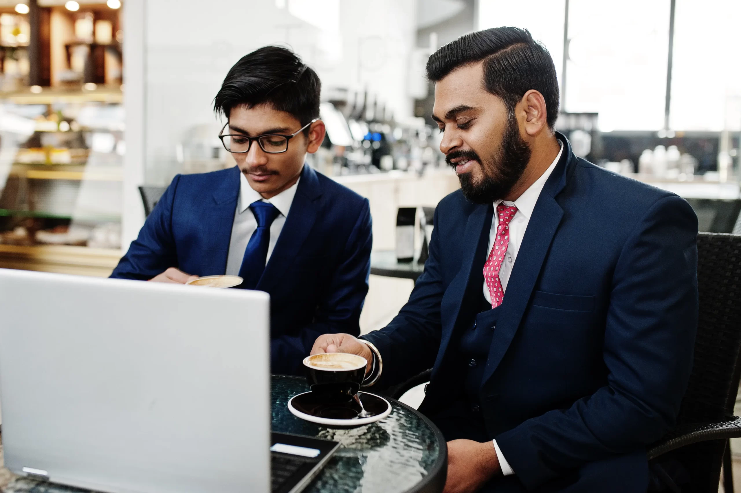 two-indian-business-man-suits-sitting-office-cafe-looking-laptop-drinking-coffee